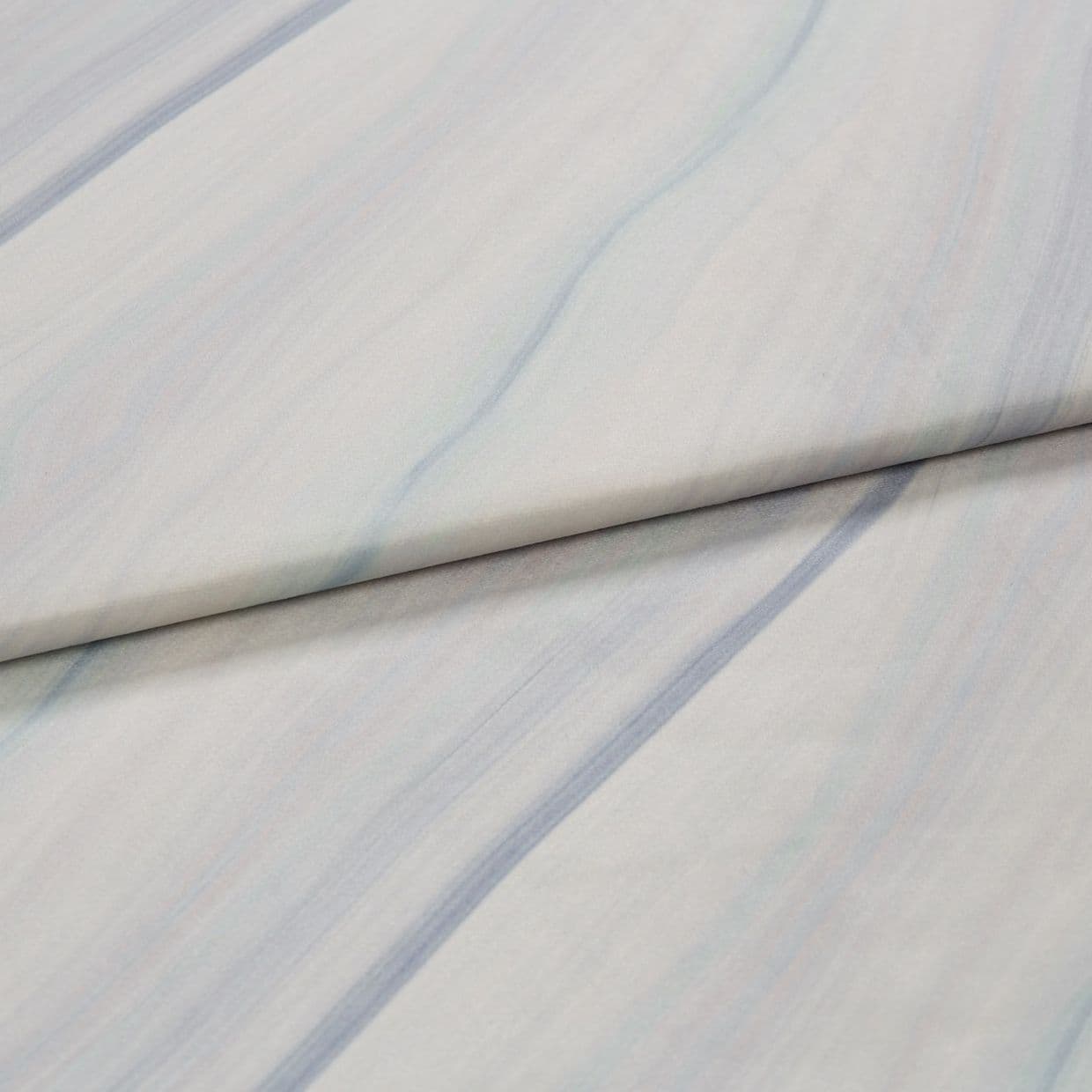 Pale marbled fabric with soft blue-gray veins, folded diagonally across the frame and lying flat on a neutral surface; diffuse, even lighting reveals subtle texture.