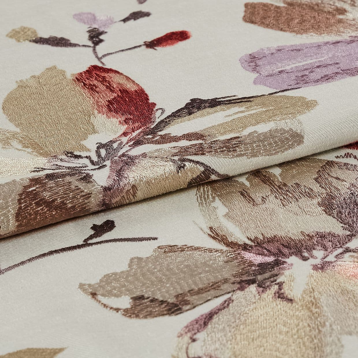 Folded cream jacquard fabric with metallic beige, mauve and red floral motifs â€” layered to reveal raised sheen and woven texture â€” close-up on flat surface under soft, even lighting.