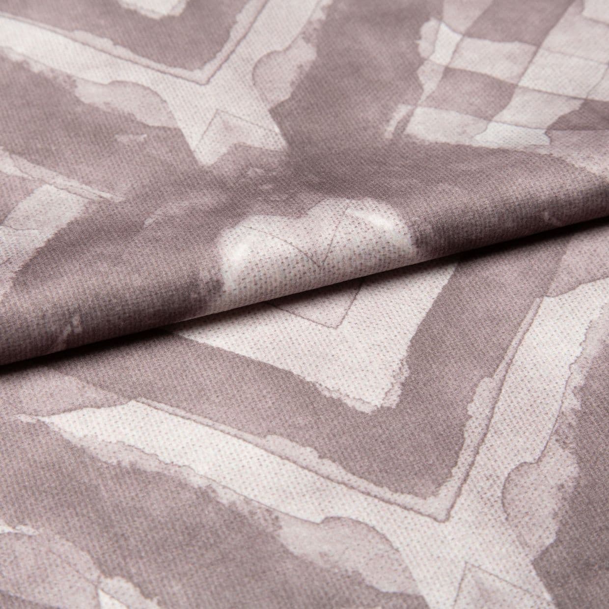 Soft woven fabric with faded mauve geometric frames and subtle heart motif (folded across the center), draped and overlapped to reveal stitched texture, close-up under even studio lighting.