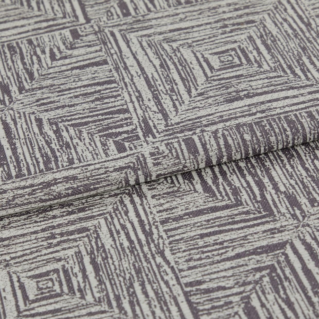 Folded woven fabric featuring a repeating distressed concentric-square pattern; a folded edge overlaps, lying flat on a neutral surface under soft, even studio lighting.