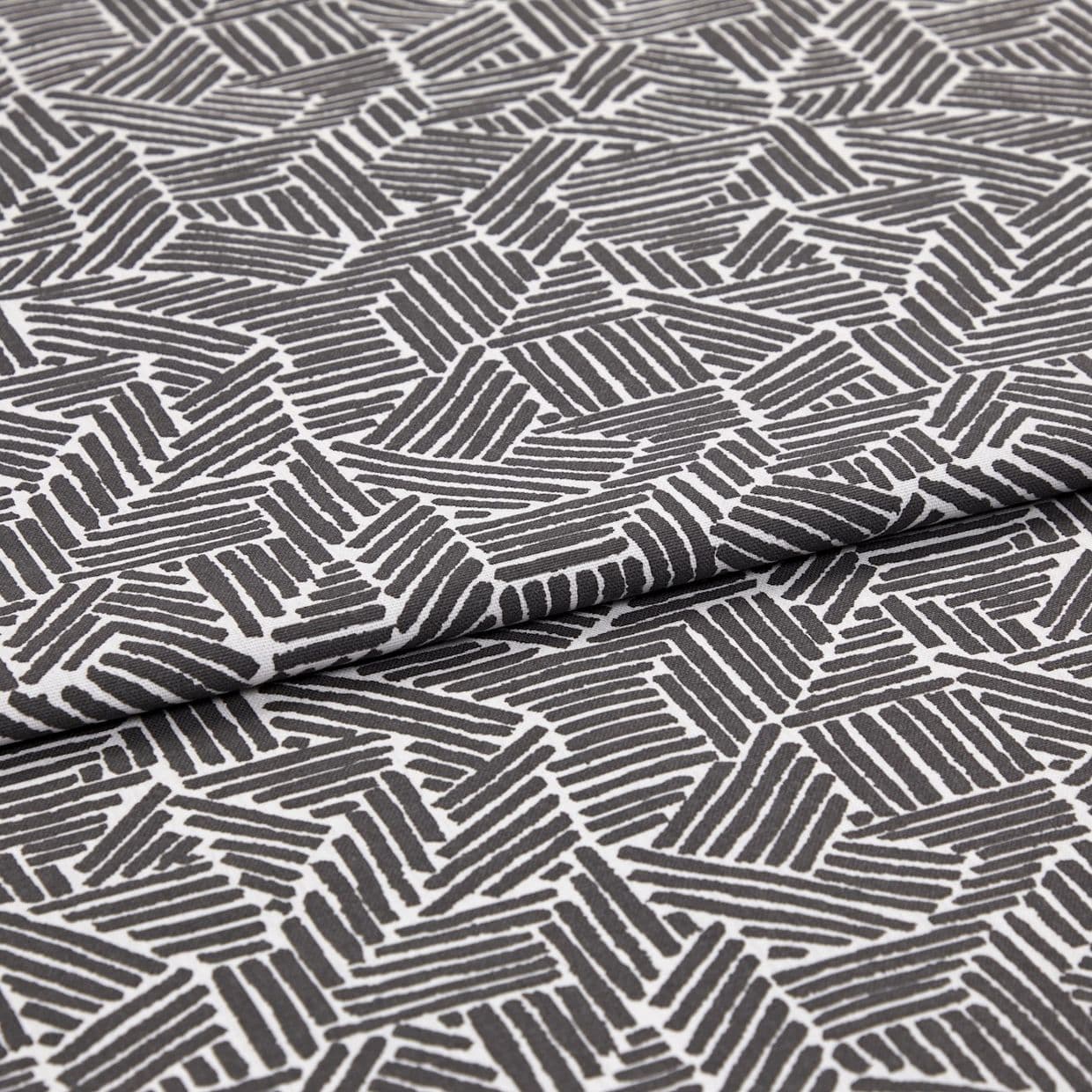 Folded patterned fabric: gray-and-white geometric print of short parallel stripes forming irregular polygons, folded across the middle. Close-up on flat surface with even studio lighting.