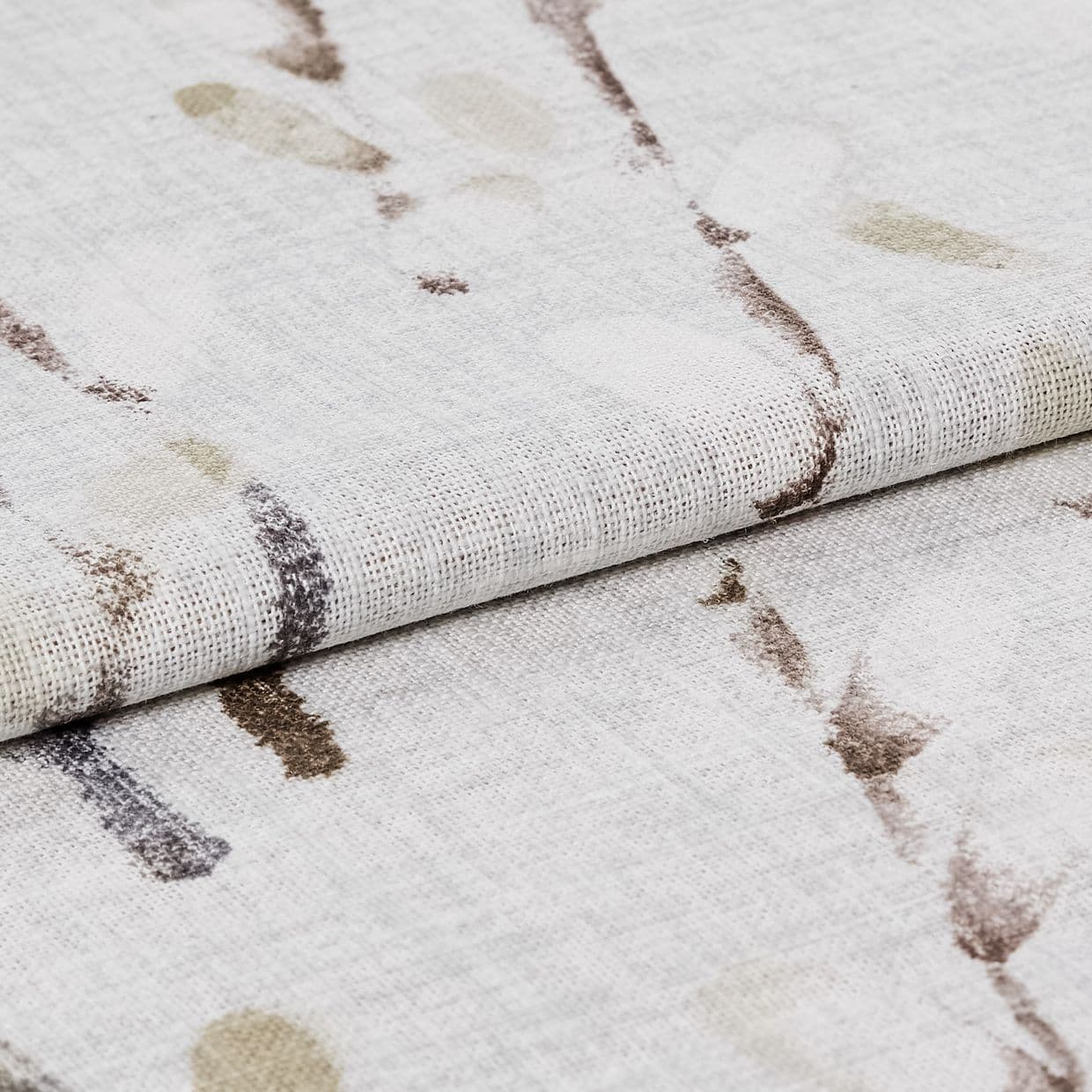 Folded woven curtain fabric with loose weave and abstract brown and beige brushstroke marks; folded edge forming a soft ridge; close-up, neutral-toned surface under diffused light.