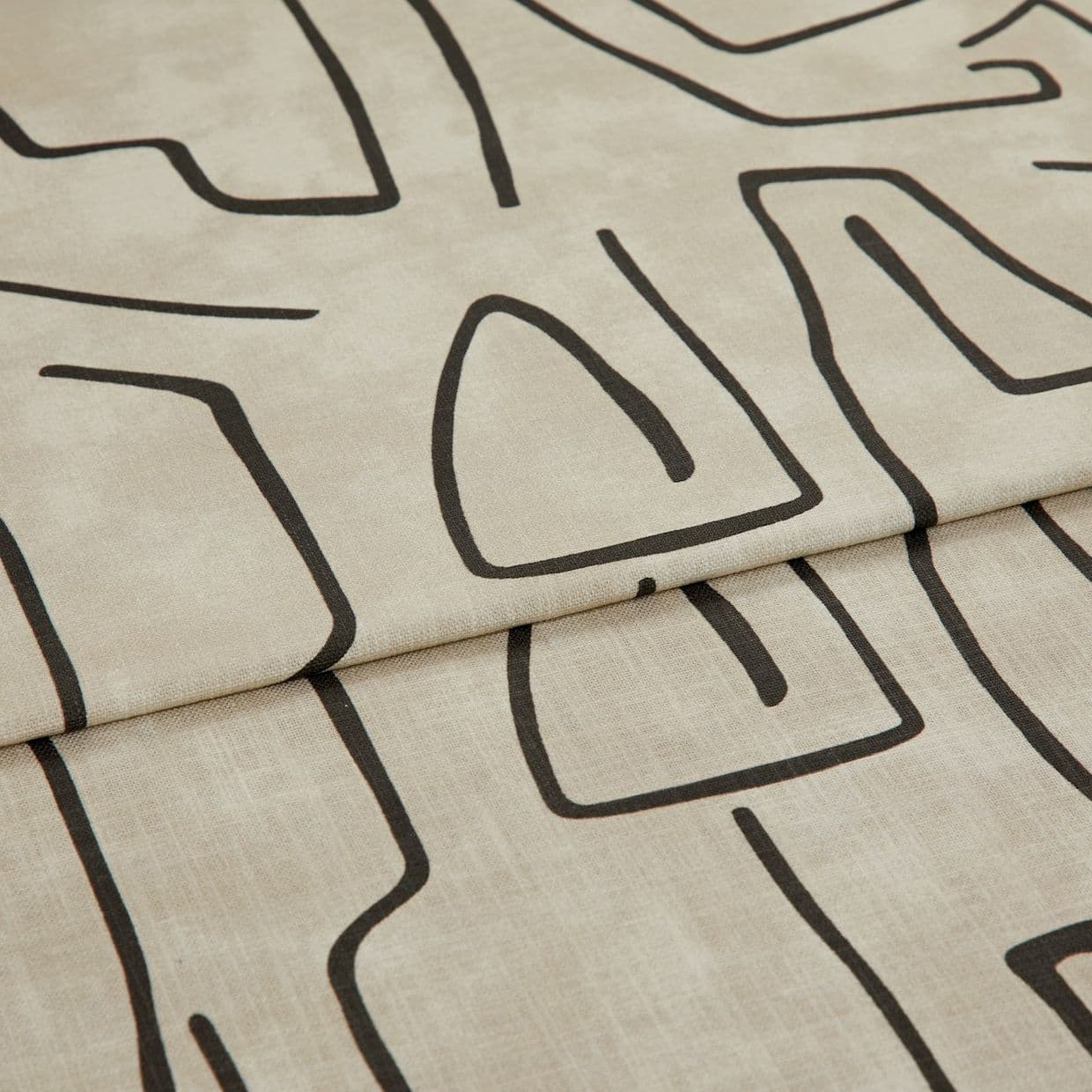 Beige linen-like curtain fabric with bold black abstract line pattern, hem visible; folded into a horizontal pleat; close-up in soft, neutral lighting showing fabric texture.