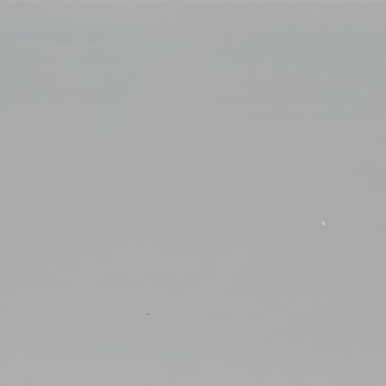 Large smooth matte gray surface with scattered tiny white specks; uniformly lit and stationary; fills frame, suggesting a neutral wall or overcast sky with soft ambient lighting.