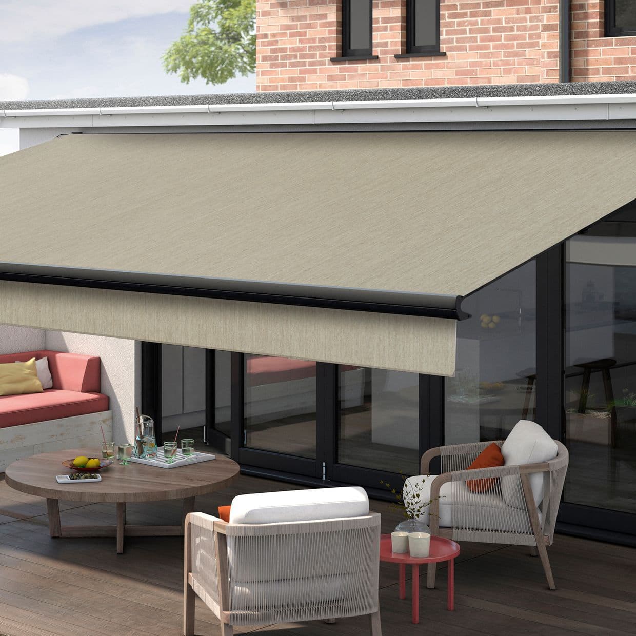 A large beige retractable fabric awning, extended from the building with a black roller front, shading a glass-door patio with wicker chairs, round wooden table, brick upper wall and daylight.