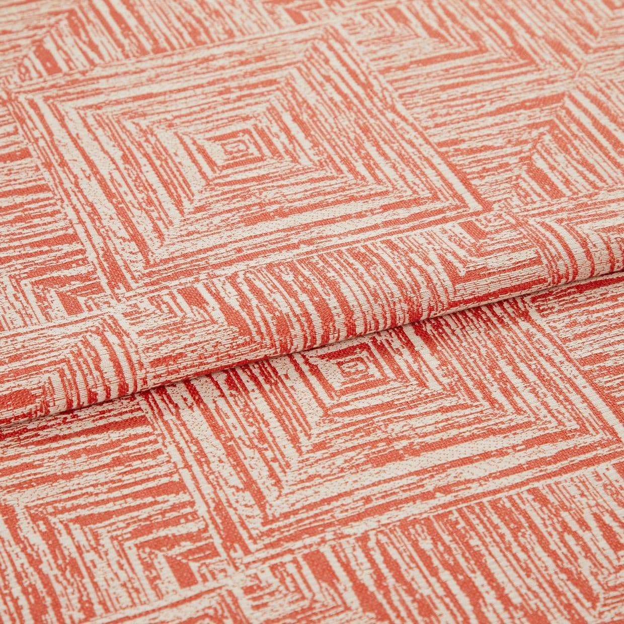 Folded coral-and-cream fabric with textured concentric-square print; a layered fold reveals repeating pattern, shown close-up on a flat surface under soft, even lighting.