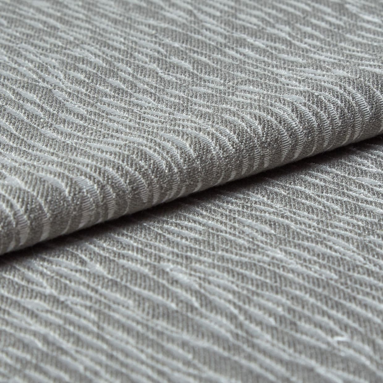 Folded grey woven fabric with raised, wavy ribbed texture (object) layered across itself (action) in a close-up, neutral-lit studio view emphasizing tactile detail (context).