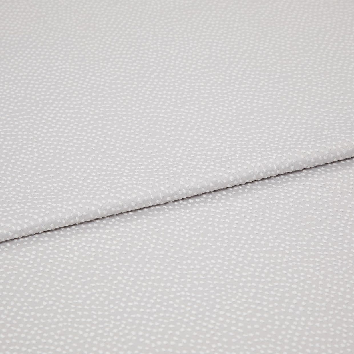 Light-gray fabric with small white dotted texture, folded diagonally with an overlapping edge; close-up view on a plain surface under soft, even lighting.