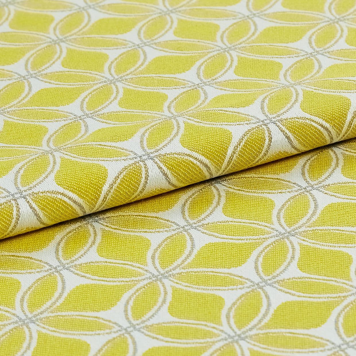 Folded yellow-green jacquard fabric with cream embroidered interlocking petal motif, close-up on a flat surface with bright even lighting, presented as a textile sample for upholstery or curtains.