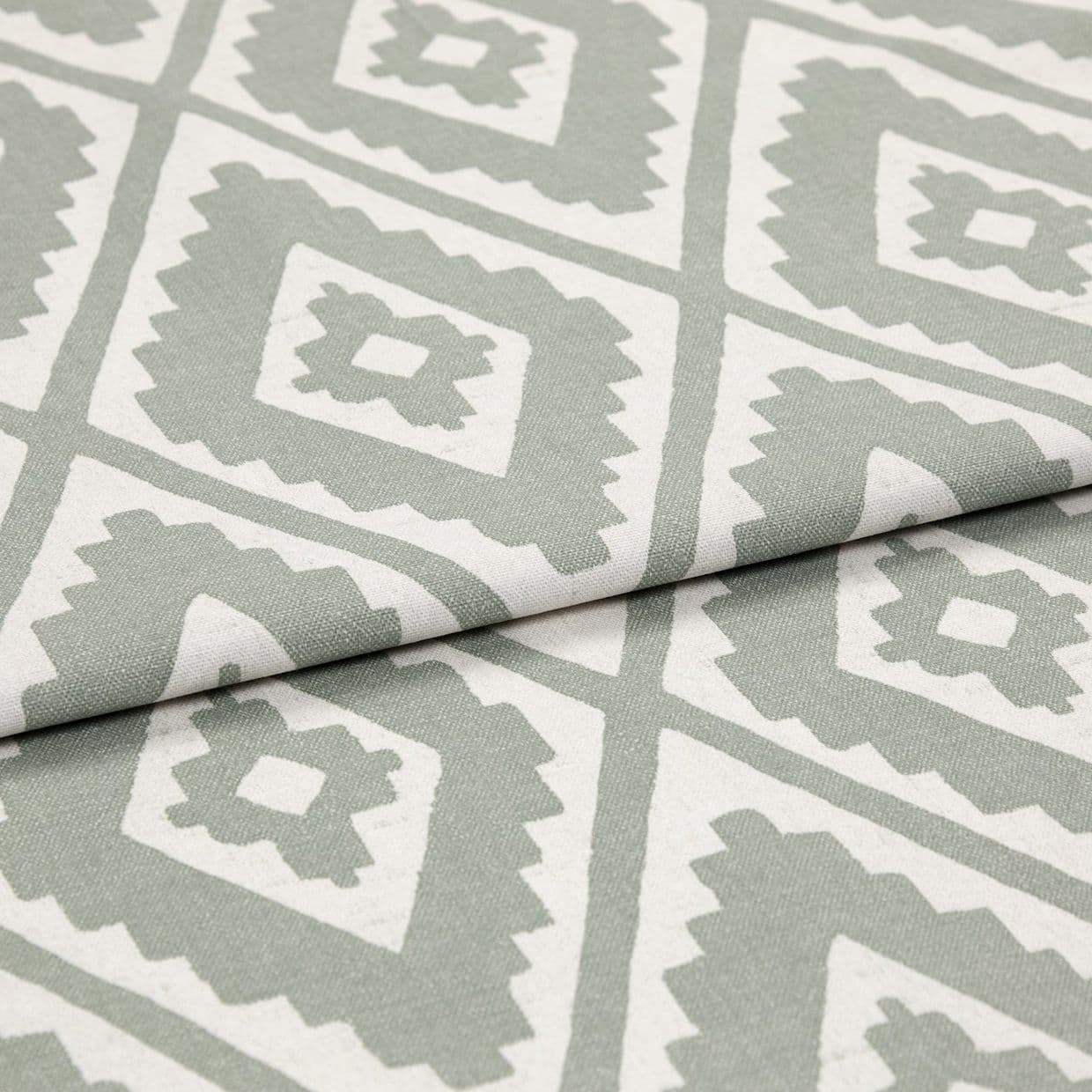 Folded woven fabric featuring repeating jagged-diamond, Aztec-like motif in sage green and off-white â€” layered across itself, lying flat in a soft, evenly lit close-up highlighting weave texture.