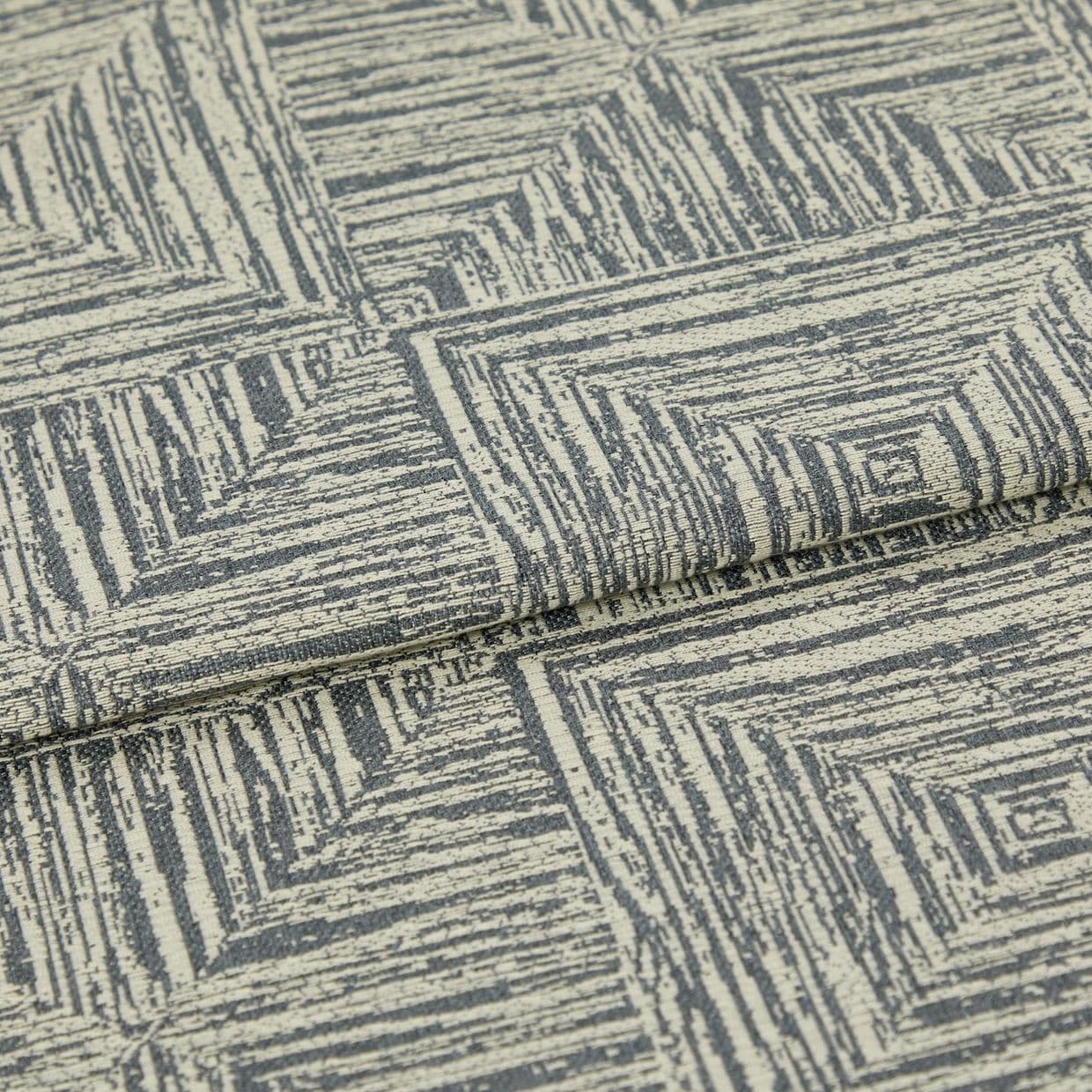 Woven upholstery fabric, cream base with gray, hand-drawn concentric-square pattern, folded over itself; photographed close-up under neutral studio lighting, showing textured weave and a layered edge.