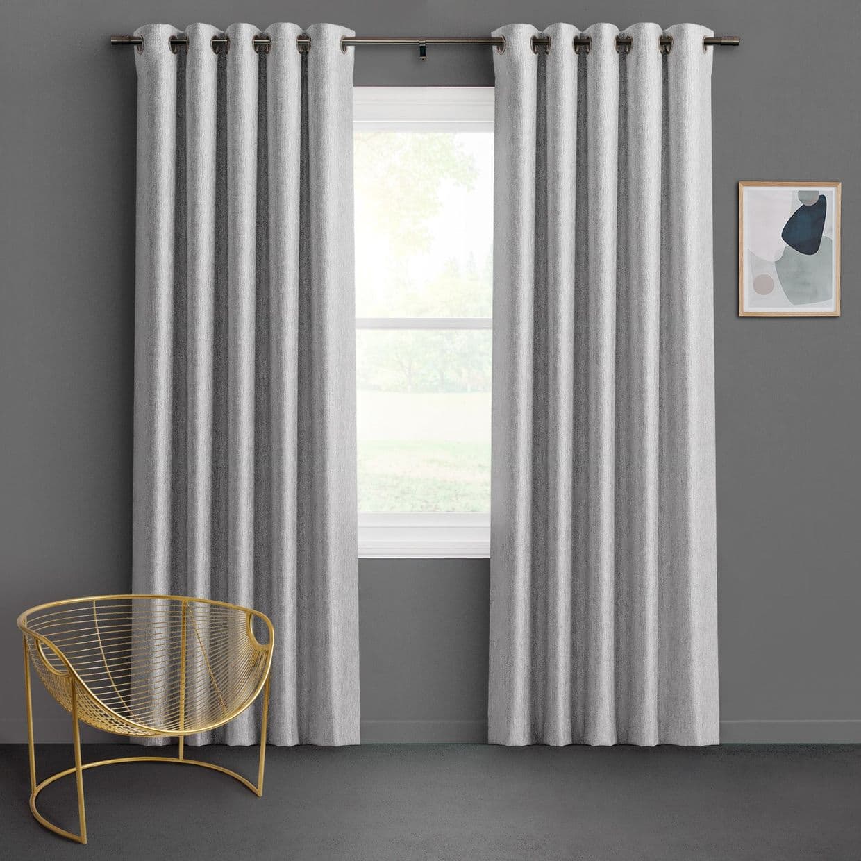Light-gray grommet-top curtains flank a central window, partially closed and filtering soft daylight; gray-walled minimalist room with a gold wire chair and small abstract wall art, faint greenery outside.