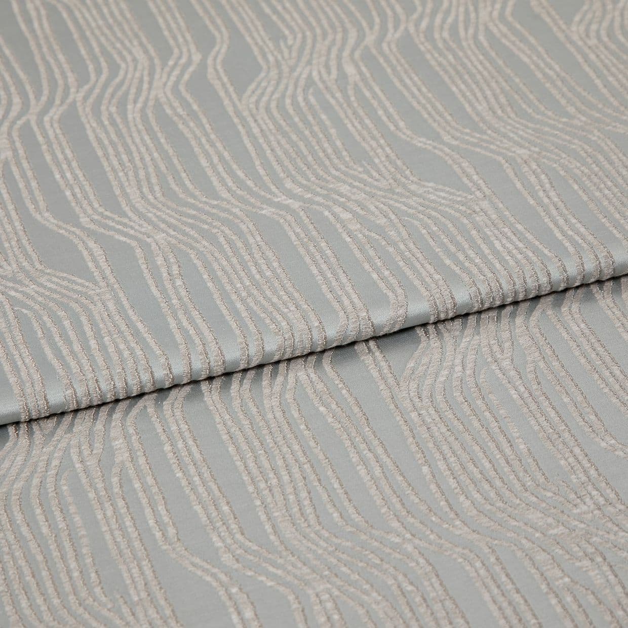 Folded patterned fabric with raised, parallel wavy chenille stripes in pale beige on a muted gray-green background; lying flat with a central fold under soft studio lighting, close-up view.