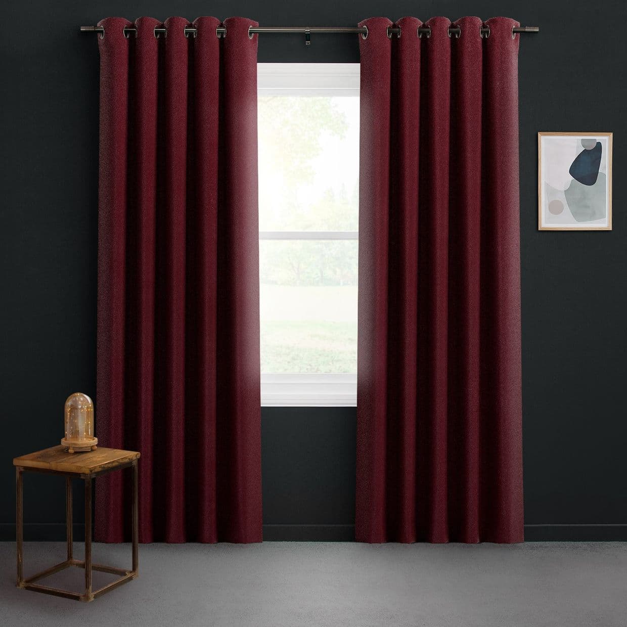 Burgundy grommet-top curtains, hung on a metal rod, slightly parted to reveal a white-framed window filtering soft daylight; dark-painted room with a small wooden side table and framed abstract art.