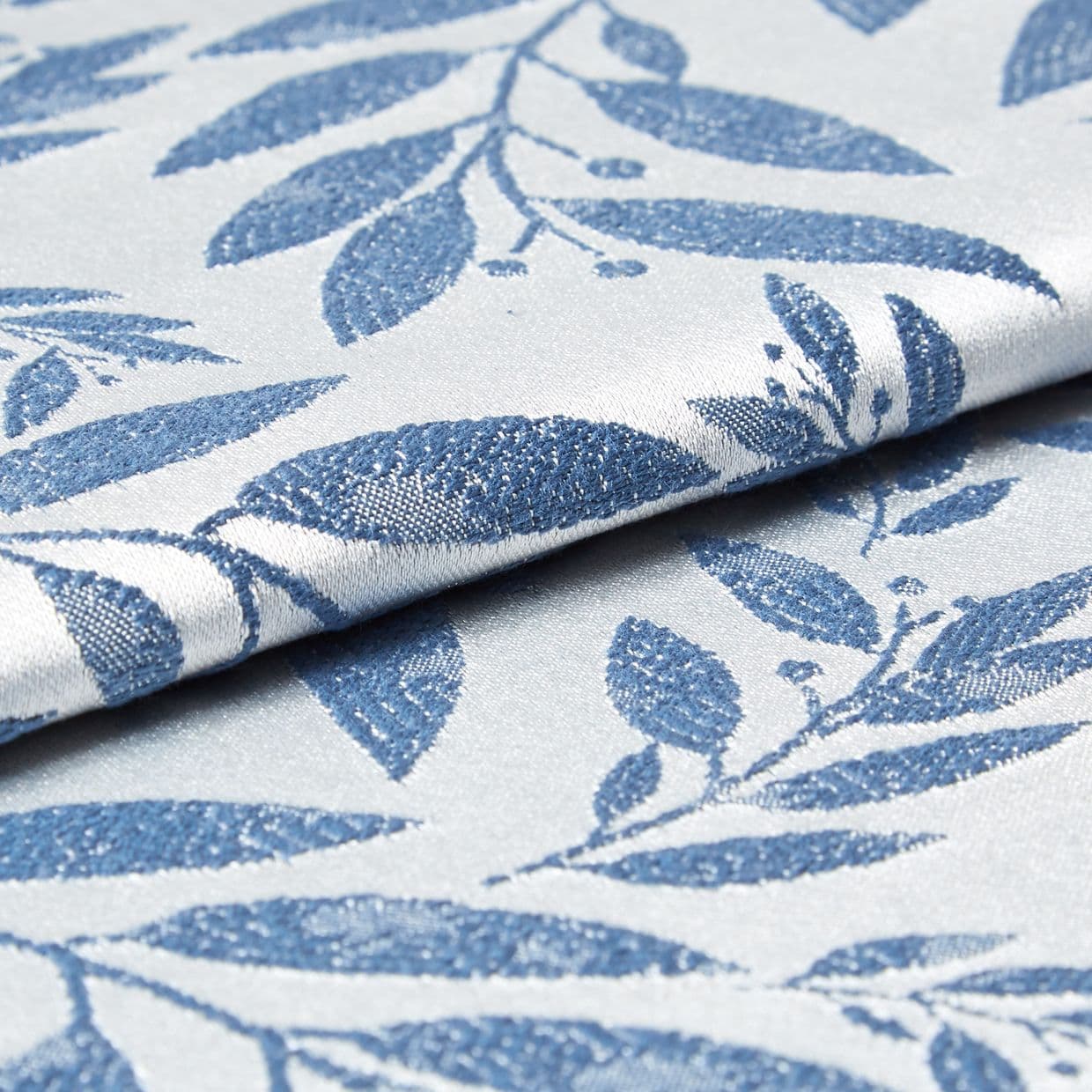 Folded woven fabric with raised blue leaf jacquard pattern; folded and overlapping, revealing textured weave and subtle sheen; close-up product-style shot with soft, neutral lighting suggesting upholstery or curtain material.
