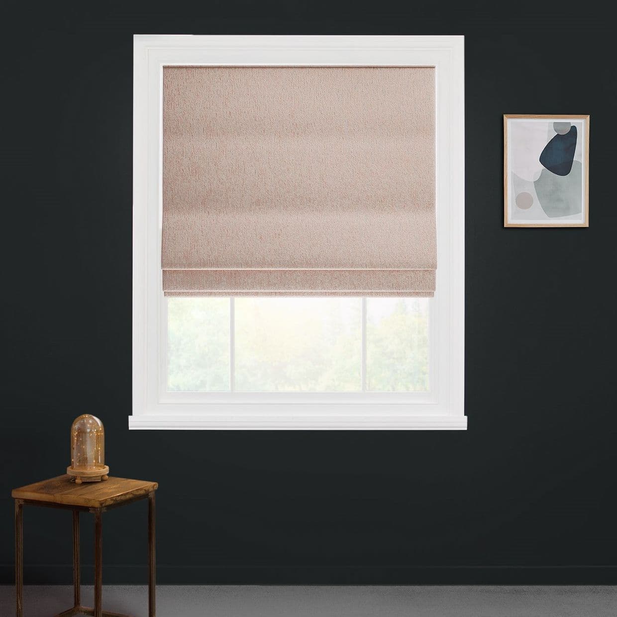 Beige textured Roman blind lowered over most of a white-framed window, its folded fabric filtering daylight into a dark charcoal room with a wooden side table and abstract wall art.