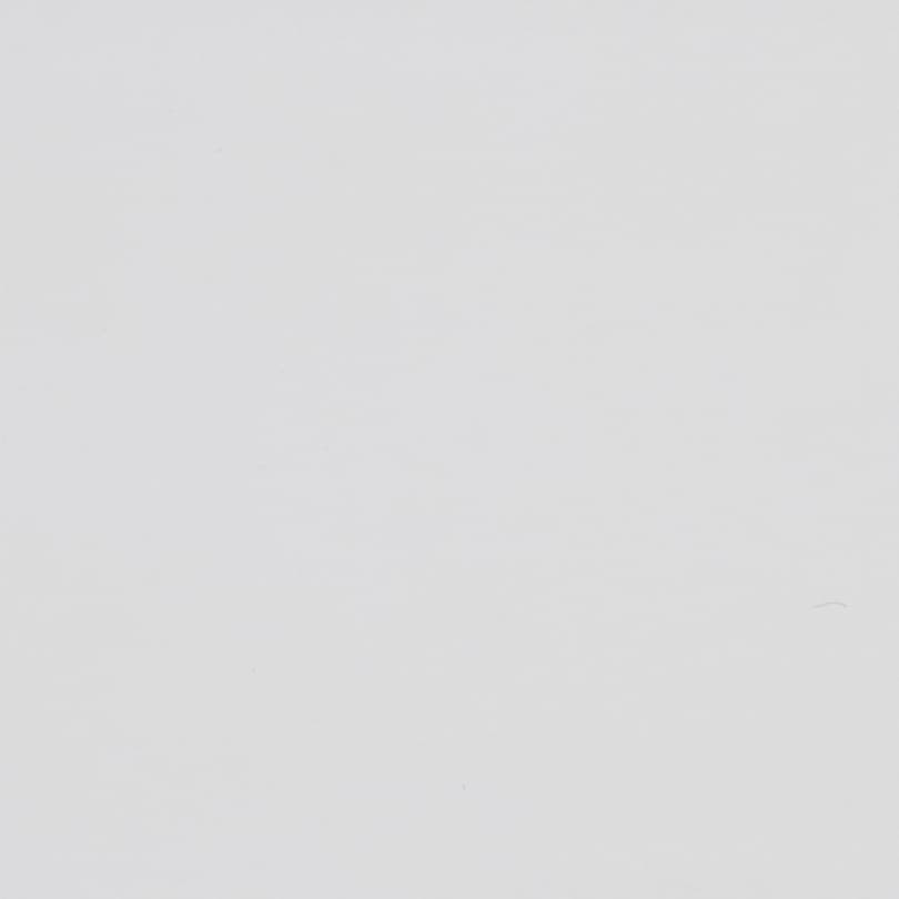 Blank off-white surface shows faint scuffs and tiny specks, evenly lit in a close-up, minimal context with subtle paper- or plaster-like texture.