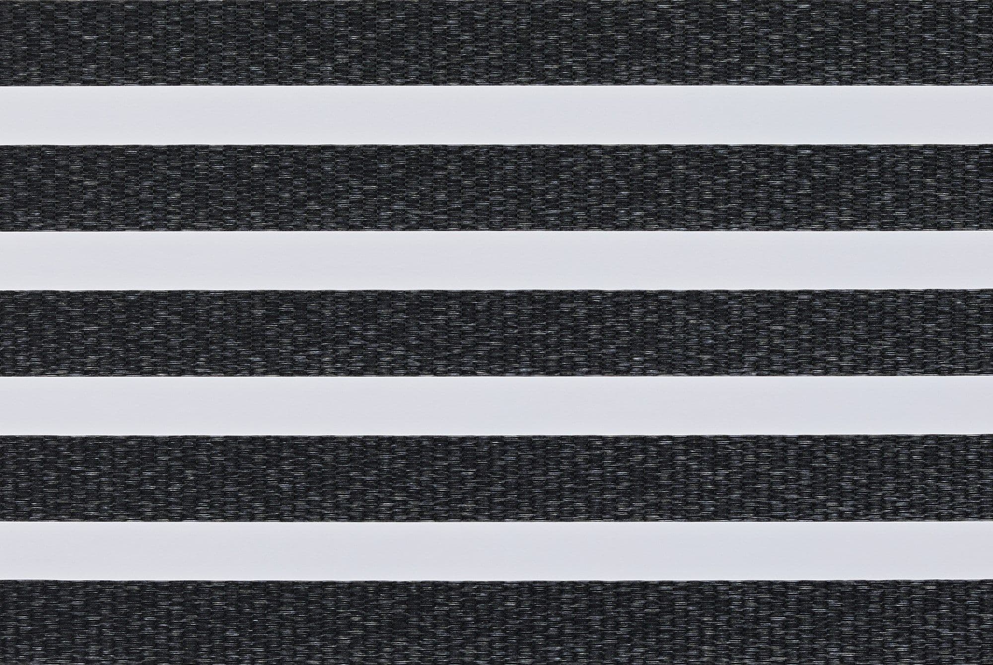 Zebra-style roller blind: alternating opaque white and textured charcoal-gray woven horizontal bands filling the frame; bands aligned to block or filter light in a close-up interior view.