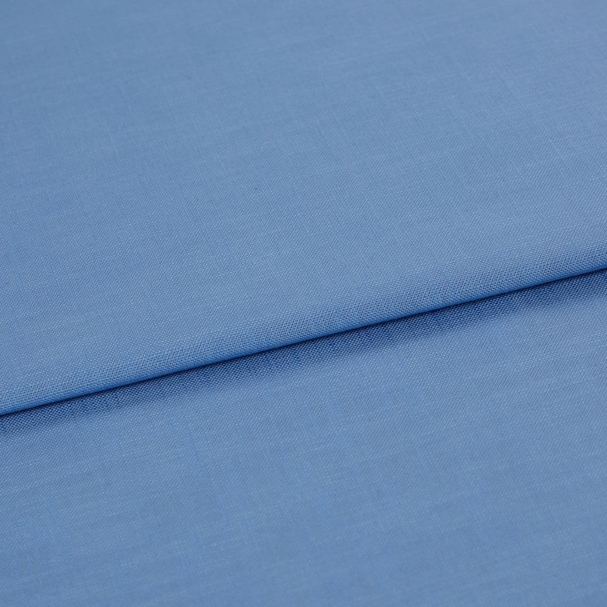 Blue woven fabric, folded with a horizontal overlap and visible fine weave; laid flat on a neutral surface under soft, even lighting in a close-up studio view.