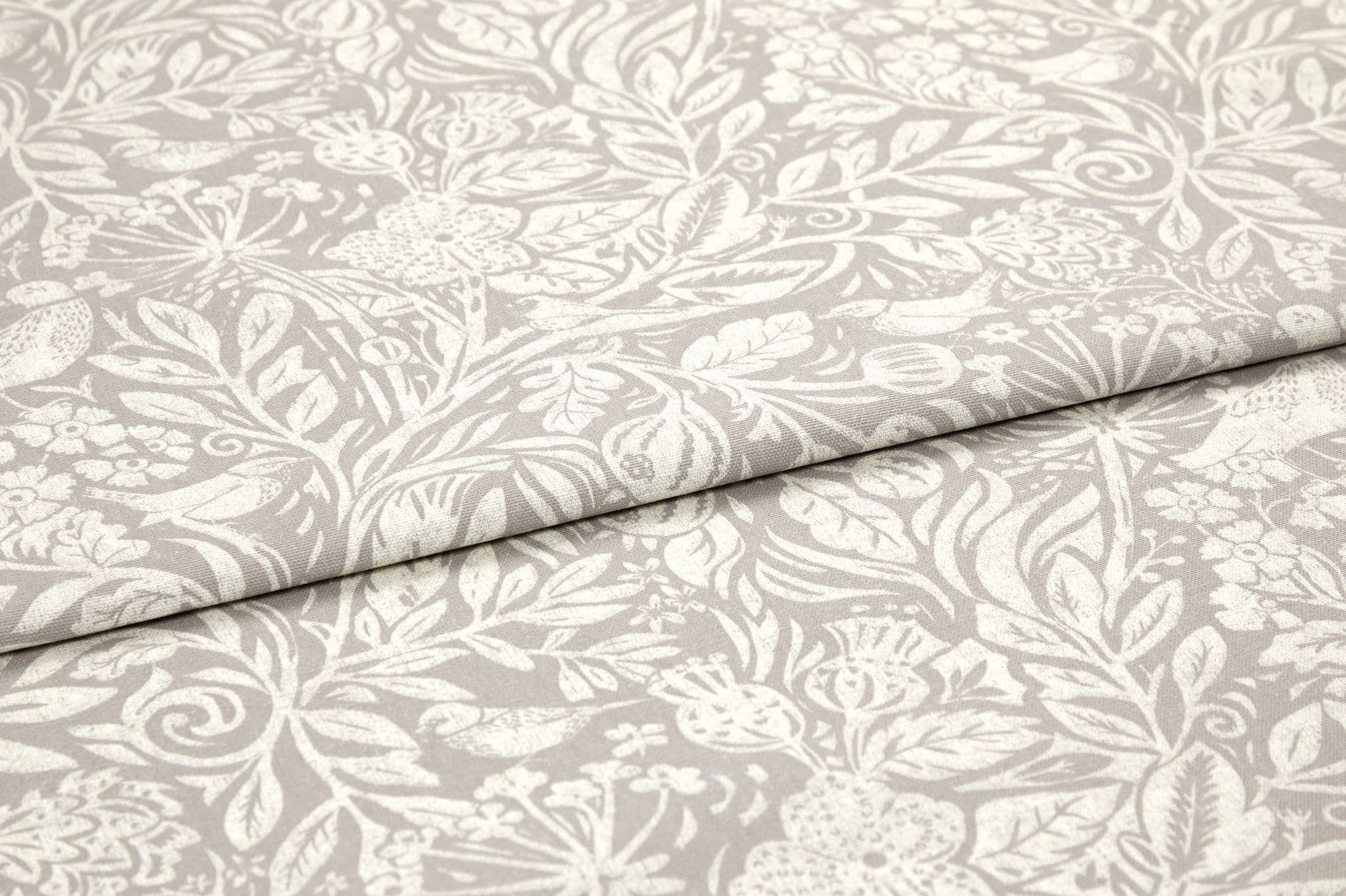 Folded beige cotton-linen fabric with white botanical print, overlapping fold across center; pattern of leaves, flowers and birds; close-up on a flat surface with soft, even lighting.