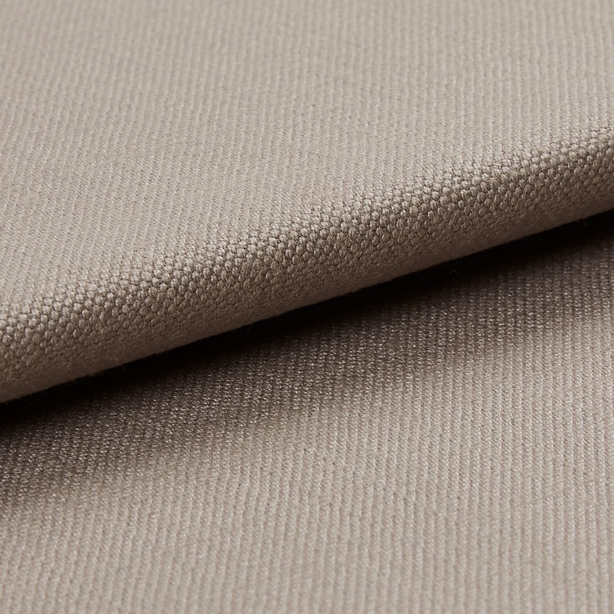 Beige tightly woven upholstery fabric, folded with an overlapping edge across the frame, revealing a pebble-like weave; close-up macro view with soft neutral lighting and plain background.