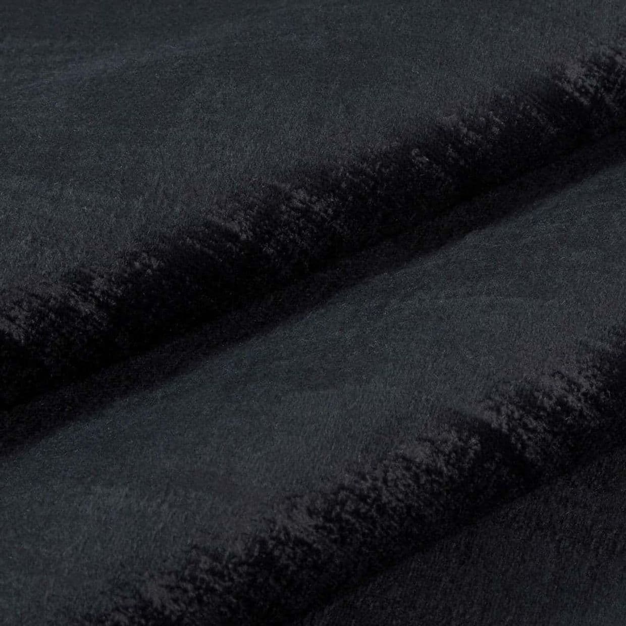 Black plush faux-fur fabric folded into two horizontal ridges, dense short pile and velvety nap; folds cast soft shadows in a close-up, evenly lit studio view.