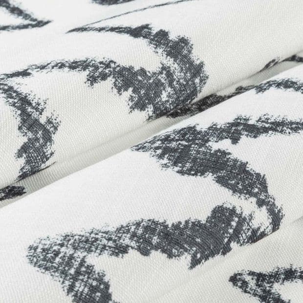 Folded white curtain-like fabric with charcoal, irregular brushstroke pattern; overlapping folds create soft ridges, showing woven texture and subtle shadows in neutral, diffuse lighting, close-up view.