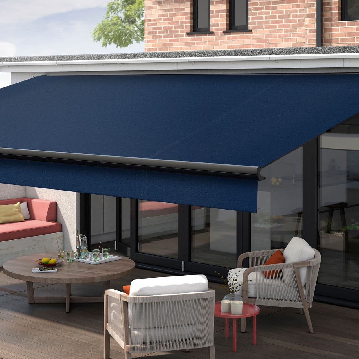 Navy blue retractable patio awning, fully extended with black roller bar, shading a glass-door terrace; outdoor seating, wooden coffee table and cushions on a sunlit deck beside a brick wall.