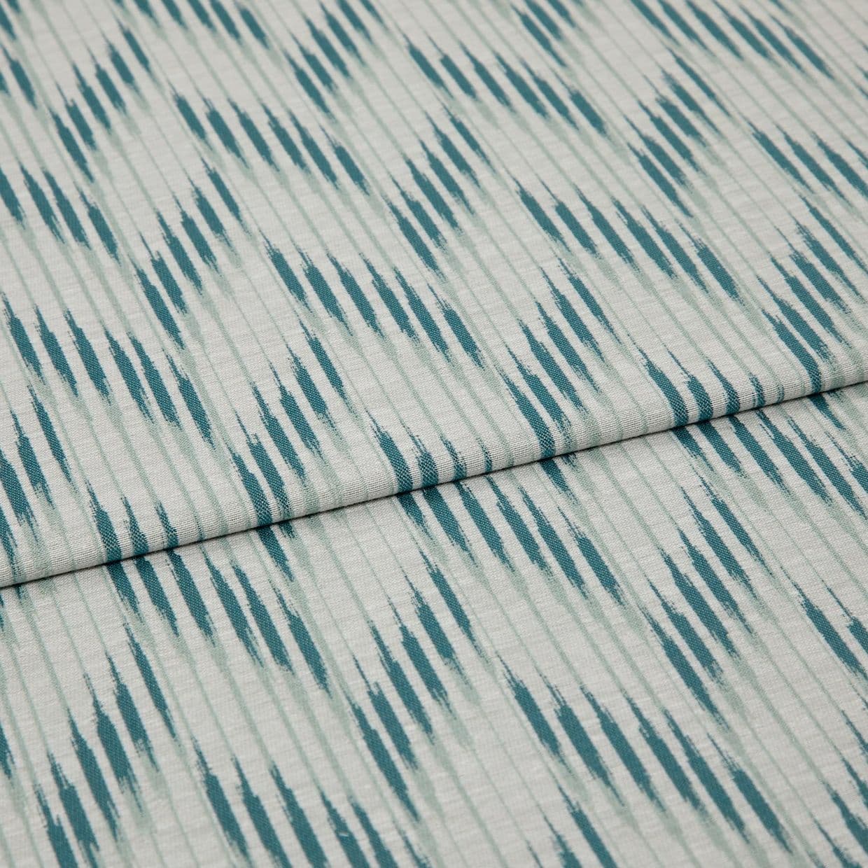 Folded woven fabric with teal ikat-like diagonal stripes and subtle vertical ribbing â€” folded once, lying flat on a neutral surface, close-up, soft even lighting.