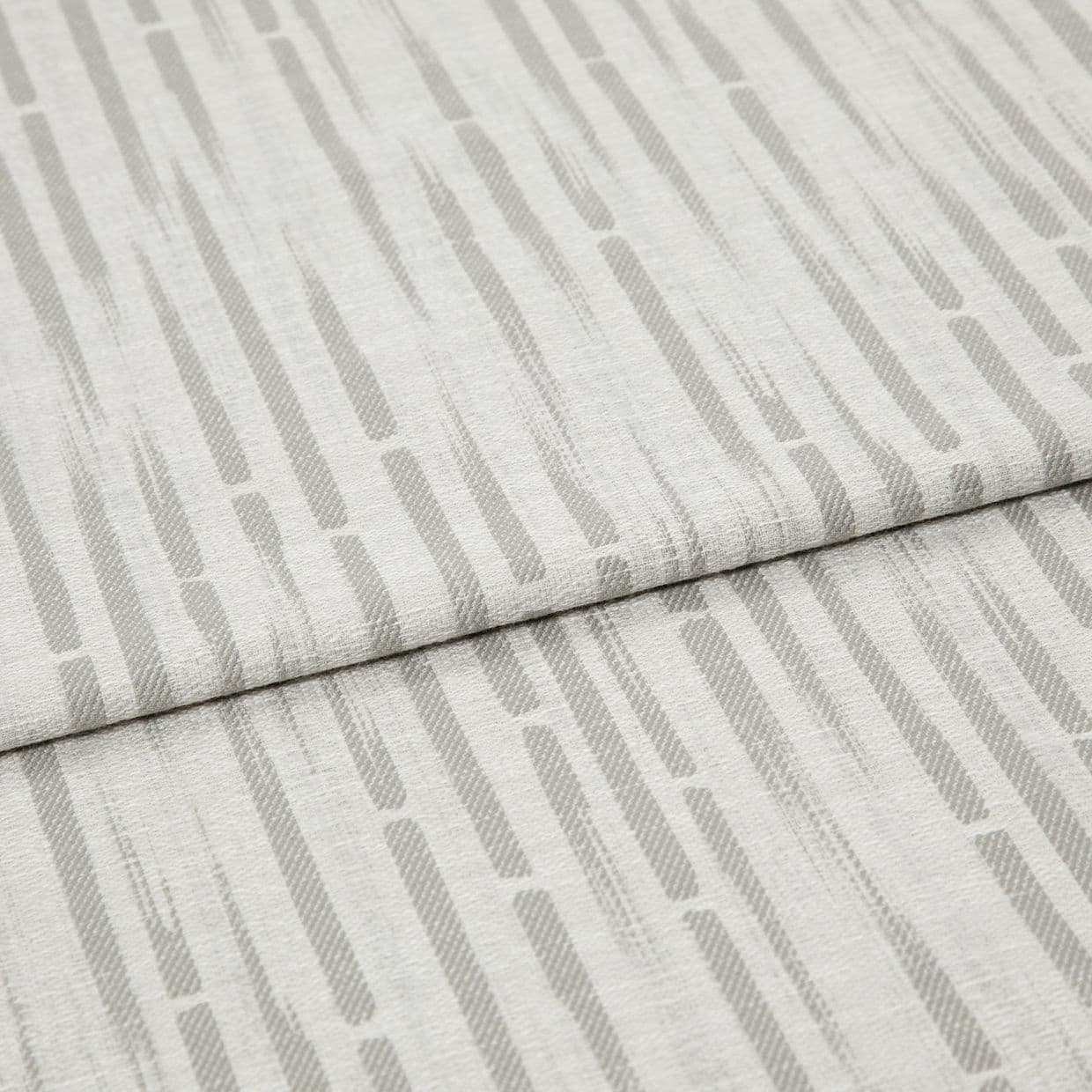 Light-gray patterned fabric, folded in overlapping panels, displaying vertical rounded dashes; close-up on textured linen-like material under soft, even lighting.