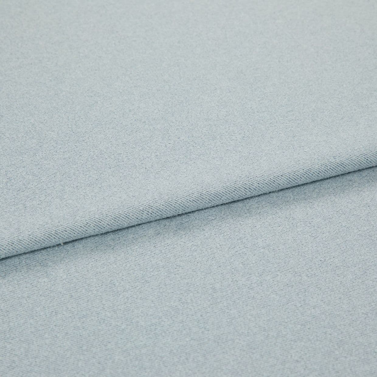 Pale blue woven fabric folded into overlapping layers; diagonal fold runs across frame, showing fine twill-like weave and subtle speckling under soft, even studio lighting.