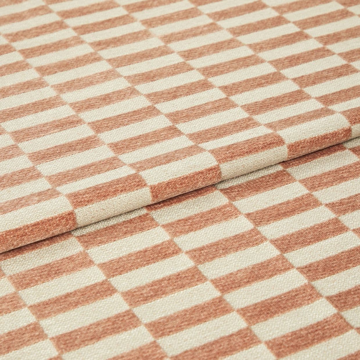 Folded woven fabric with peachâ€‘terracotta and cream rectangular stripe pattern, textured surface; layered folds overlapping; close-up studio-lit view showing a textile sample and detailed weave.