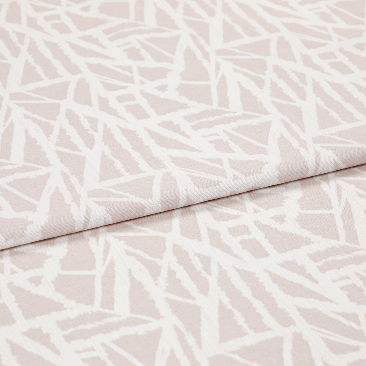 Pale pink woven fabric with white abstract angular lines (object), folded over itself (action), shown in a studio-lit close-up highlighting the textileâ€™s texture and overlapping layer (context).