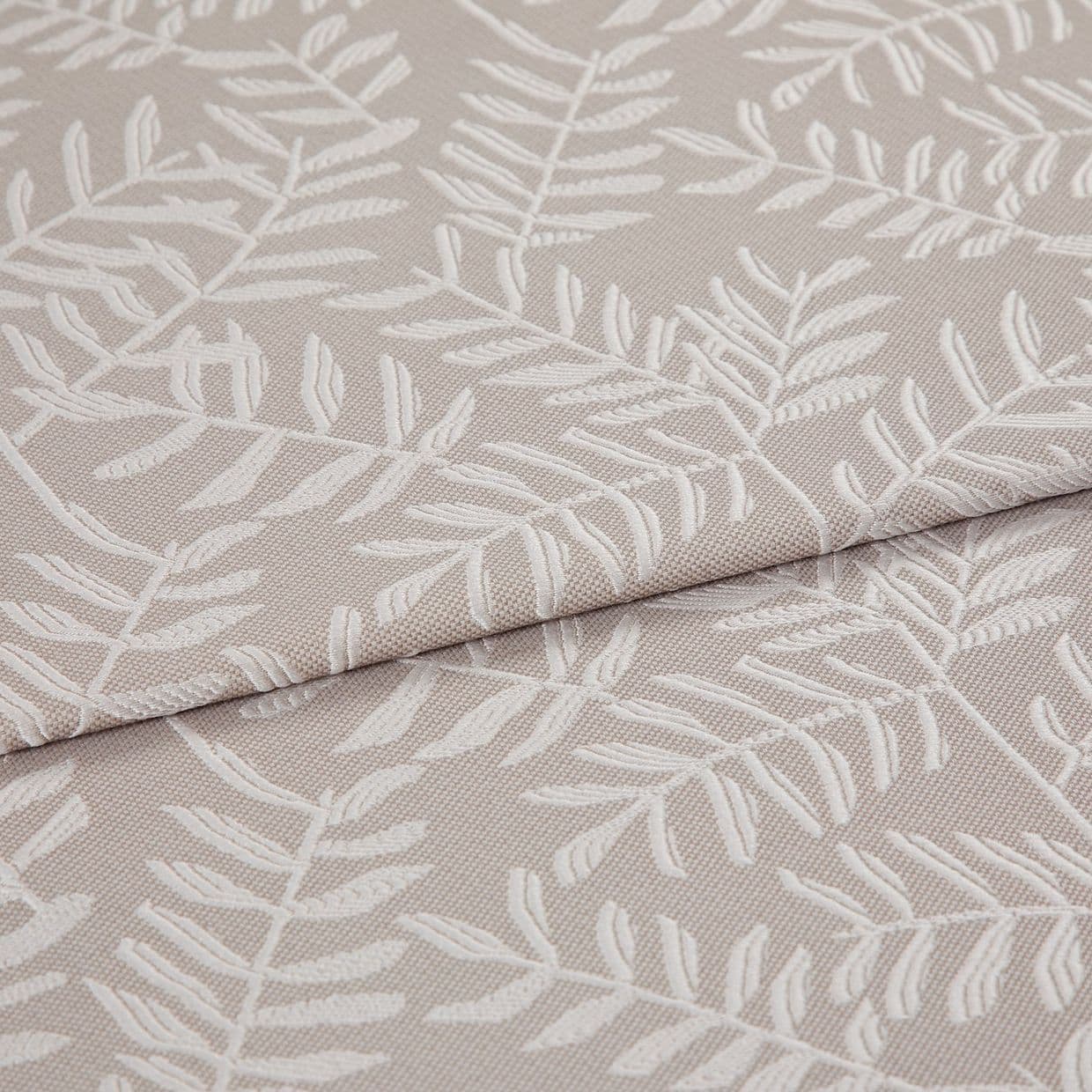 Beige jacquard fabric with raised white fern motif; folded and overlapped; close-up of an upholstery/curtain sample on a flat surface under soft, neutral lighting.