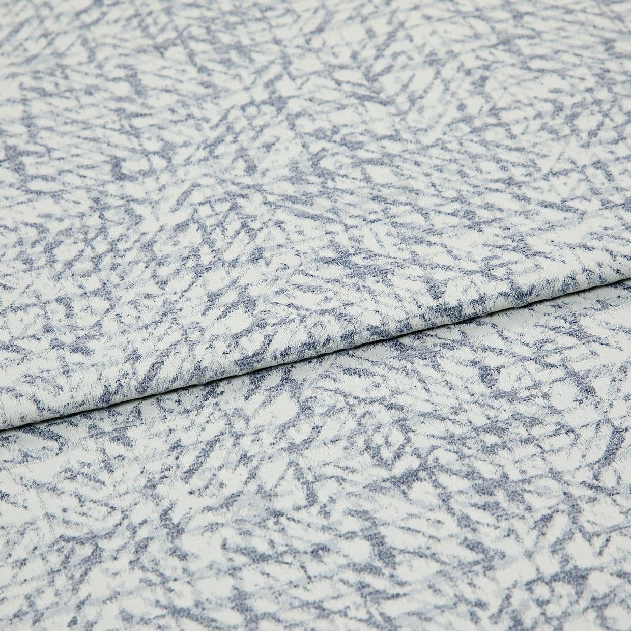 Light blue-and-white patterned fabric folded once, overlapping; textured woven surface with irregular, fern-like striations, photographed close-up under even studio lighting.
