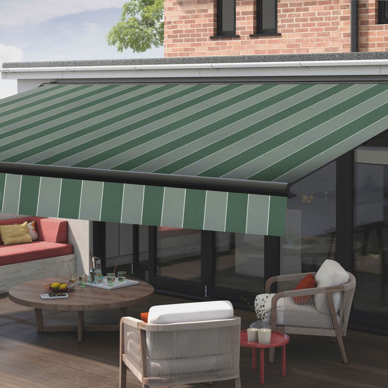 Green-and-light-green striped retractable awning, fully extended with matching valance; shading a wooden-deck patio with wicker chairs, round coffee table, and sliding glass doors beneath a brick upper wall.