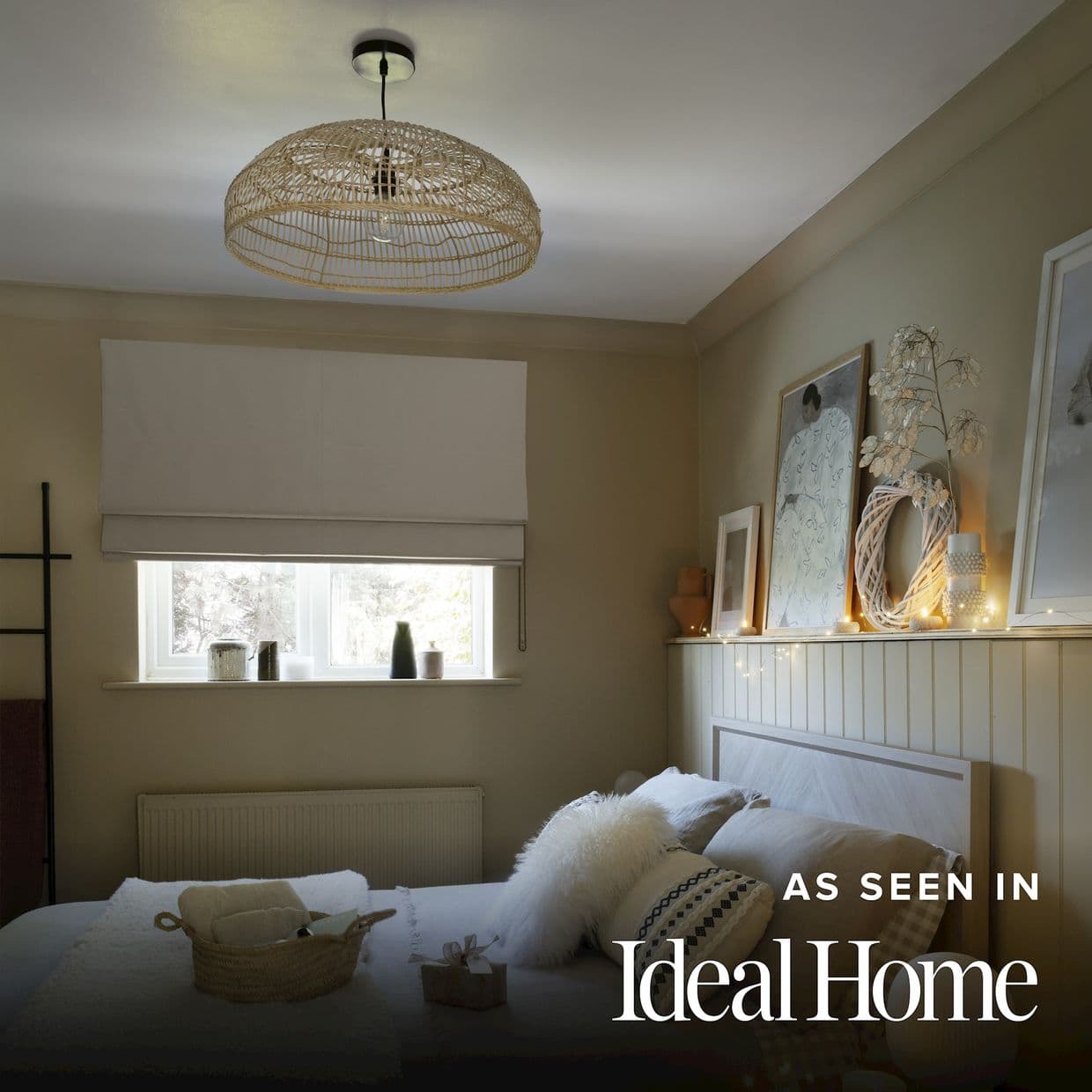 A white Roman blind lowered across a small rectangular window, diffusing soft daylight; in a neutral-toned bedroom with a woven pendant lamp, wooden headboard, cushions and a fairy-lit shelf with framed art and ornaments.

AS SEEN IN Ideal Home