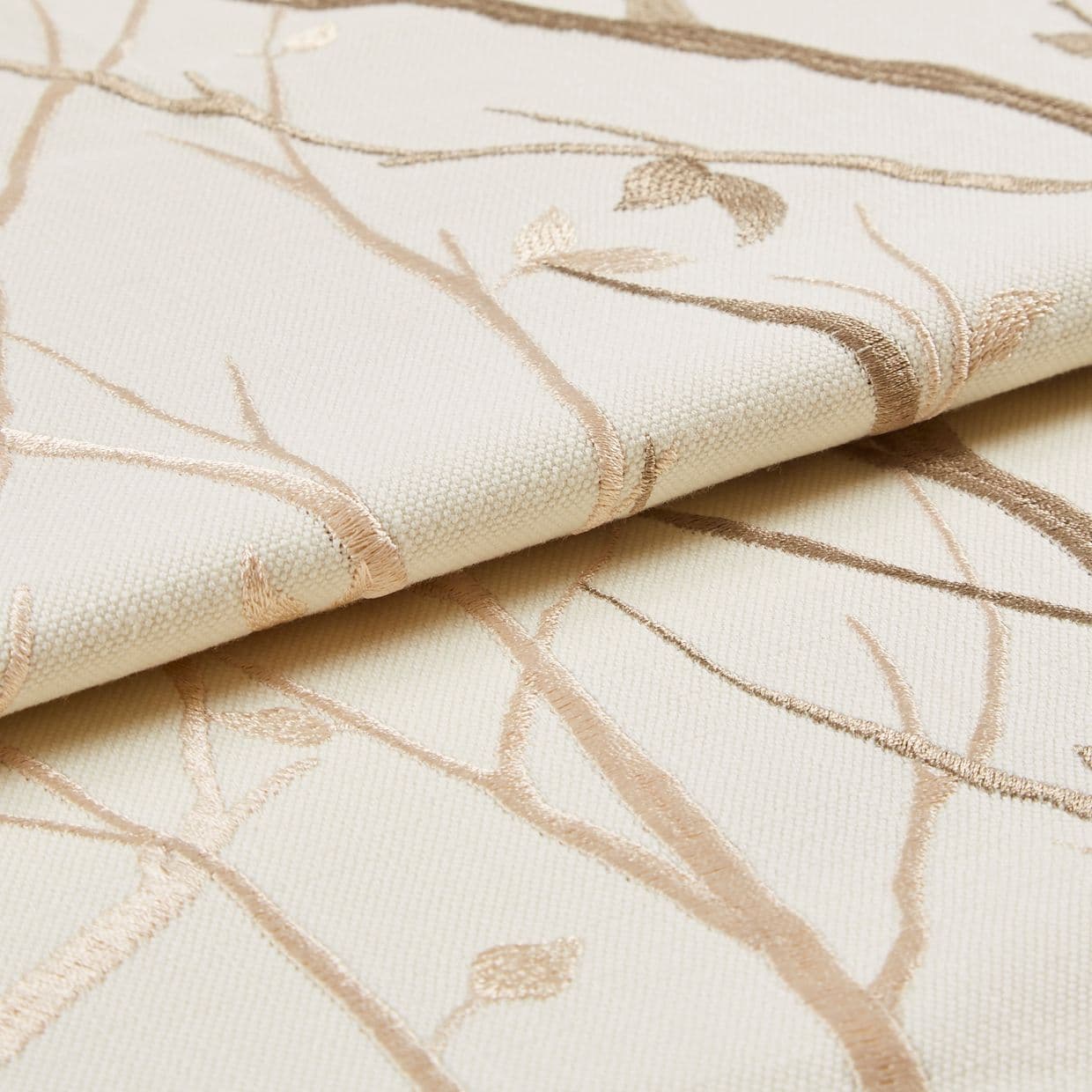 Cream woven fabric with beige embroidered branches (curtain sample), folded to show raised embroidery and textured weave; close-up studio setting with soft, neutral lighting.