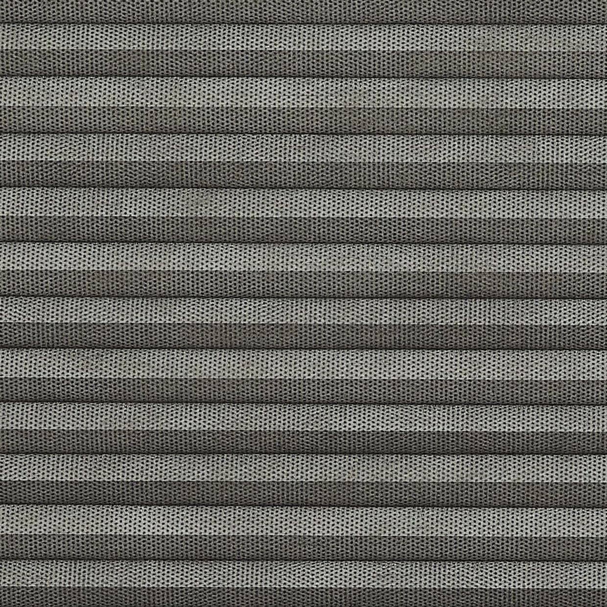 Grey pleated cellular blind, fully closed, narrow horizontal folds with perforated textured fabric; filtering light and covering a window in a softly lit interior, no visible view.