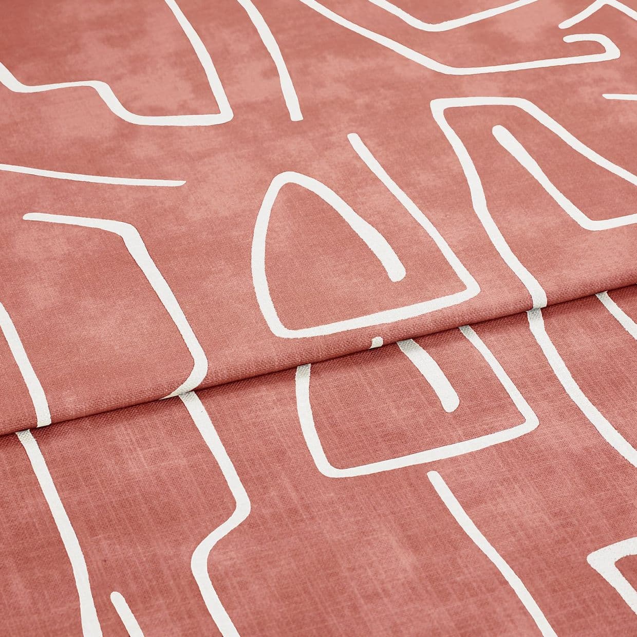 Folded patterned fabric: a roseâ€‘terracotta curtain-like textile with white abstract line motifs, folded once across the frame. Close-up studio view emphasizing soft woven texture and matte finish.