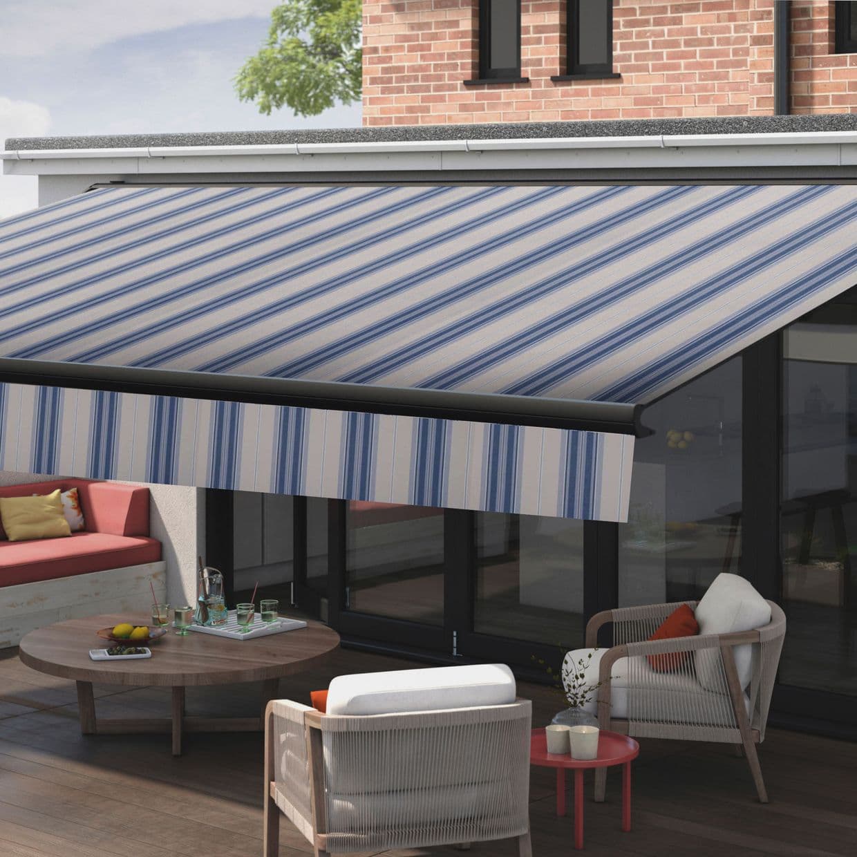 Striped blue-and-white retractable awning extended over a patio, casting shade; patio contains cushioned seating, round wooden coffee table with drinks, glass doors and brick house exterior under daylight.
