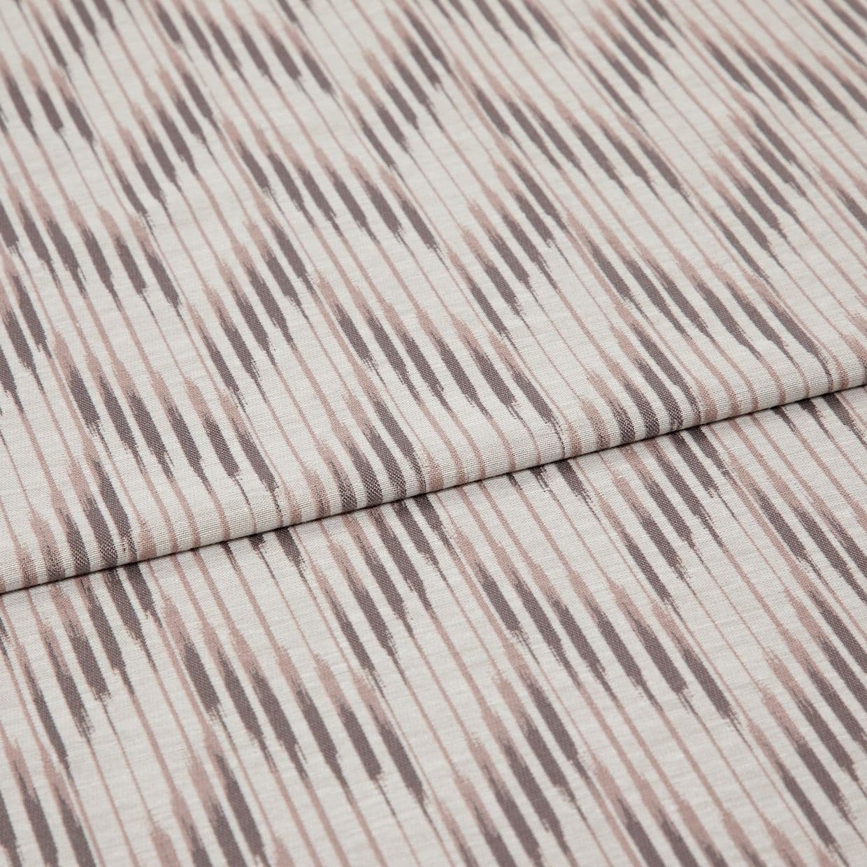 Folded patterned fabric with diagonal ikat-style stripes in muted taupe and blush lies folded across the frame, showing woven texture and subtle vertical lines in a studio-lit close-up.