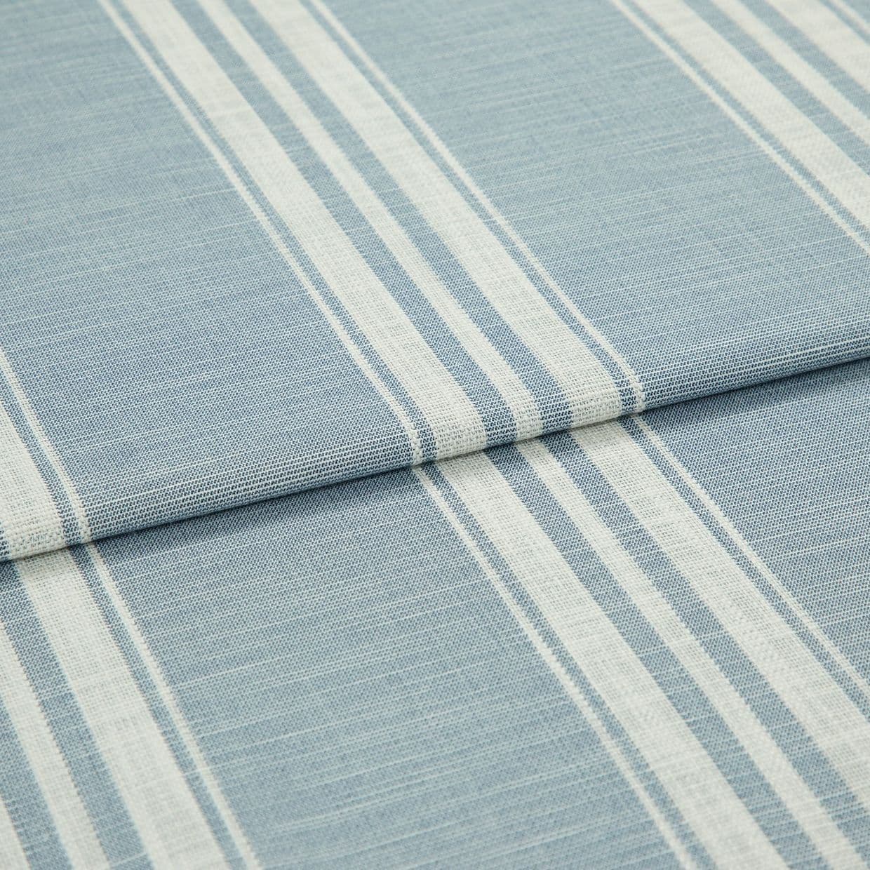 Blue-and-white striped woven fabric (curtain sample) folded into layers; vertical white stripe bands on pale blue ground, textured weave visible, close-up on flat surface under soft, even lighting.