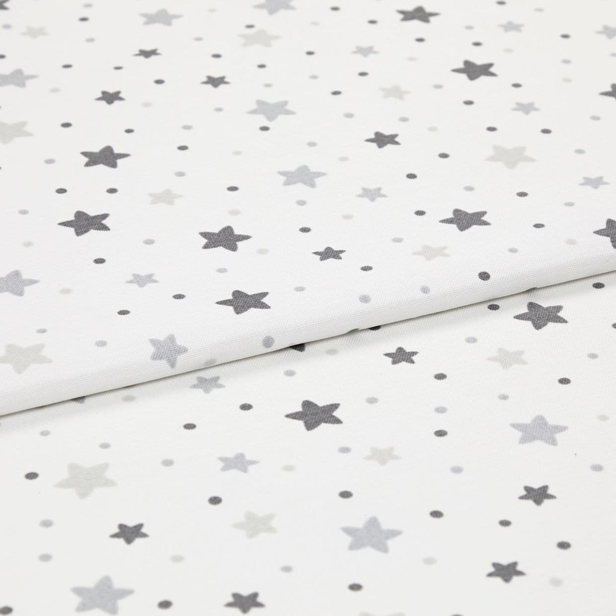 White cotton fabric patterned with scattered grey stars and small dots, folded and layered on itself; photographed as an evenly lit close-up, resembling a nursery textile sample.