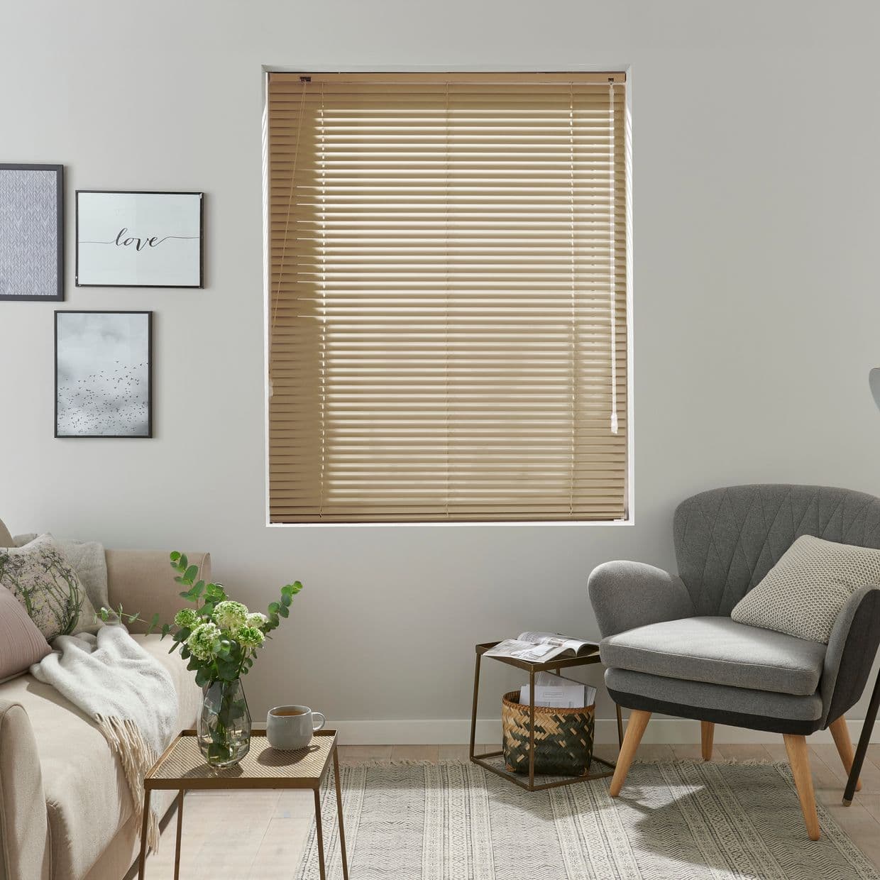 Beige horizontal slatted blinds, fully lowered with pull cords at right; closed, filtering soft daylight; neutral living room with sofa, armchair, side tables, framed art and vase.

love