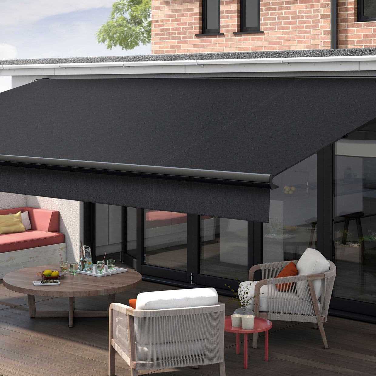 A large black retractable fabric awning, fully extended from the roof edge with a rounded front bar, shading a ground-level glass patio; daytime outdoor seating area on a wooden deck.