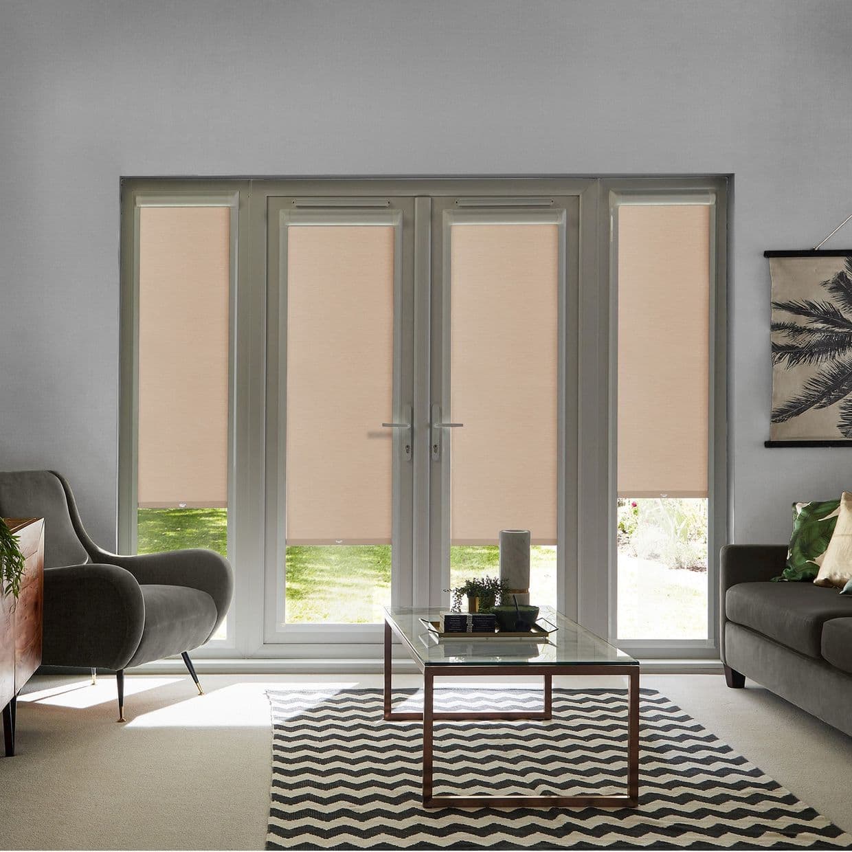 Beige roller blinds cover four tall French-style patio doors and sidelights, mostly lowered and filtering soft daylight into a modern living room with gray sofas, glass coffee table, and chevron rug.