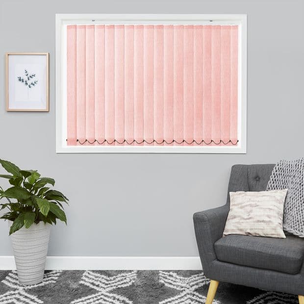 Pink vertical blinds covering a rectangular window, closed with scalloped weighted bottoms; filtering soft light into gray living room with potted plant, framed art, patterned rug, and upholstered armchair.