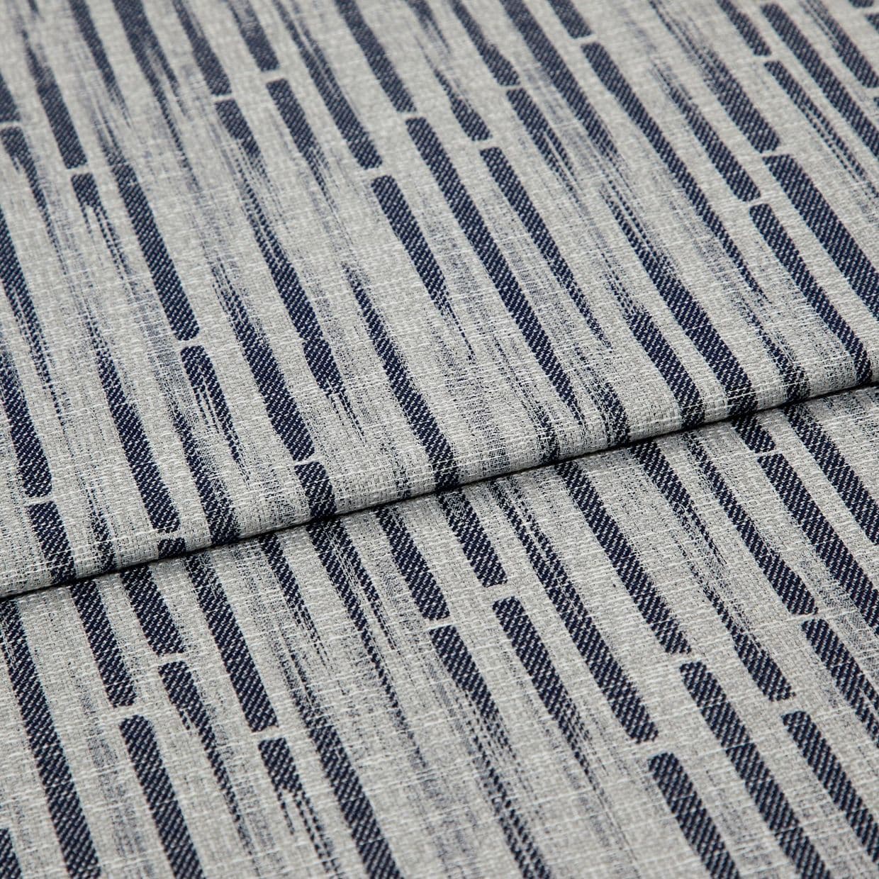 Gray woven fabric with textured weave and vertical navy elongated-dash pattern, folded across center; close-up on a flat surface showing fibers and subtle shadowing in soft, even lighting.