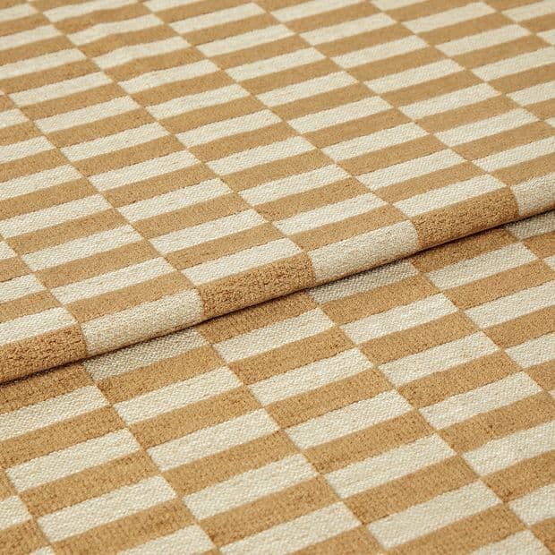 Woven beige-and-cream checkered fabric folded to create an overlapping edge, close-up studio-lit view highlighting the textured weave and repetitive rectangular pattern.